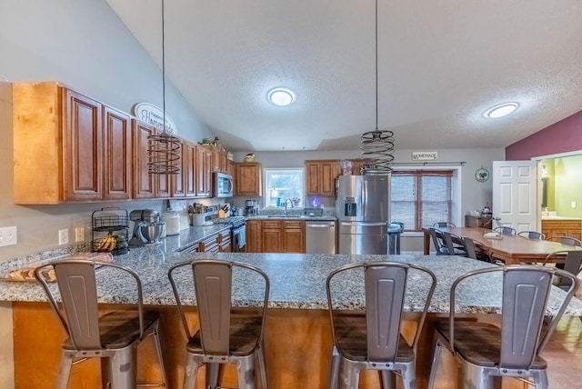 kitchen featuring pendant lighting, a kitchen breakfast bar, sink, vaulted ceiling, and appliances with stainless steel finishes