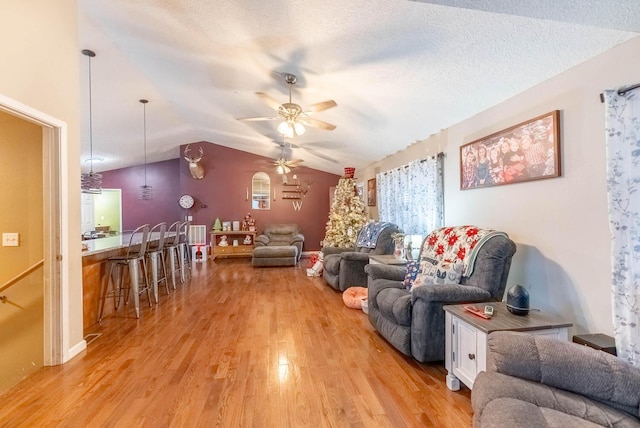 living room featuring a textured ceiling, light hardwood / wood-style floors, vaulted ceiling, and ceiling fan