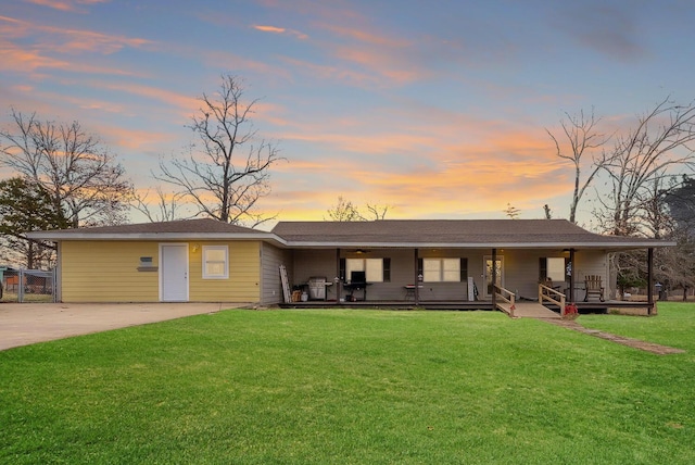 back house at dusk featuring a lawn and covered porch