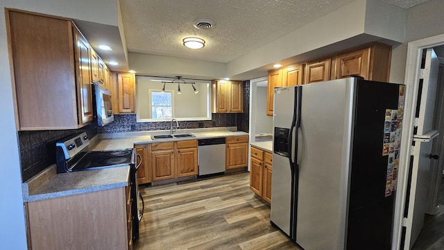 kitchen with backsplash, sink, a textured ceiling, light hardwood / wood-style floors, and stainless steel appliances