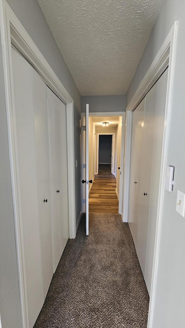 corridor with dark carpet and a textured ceiling