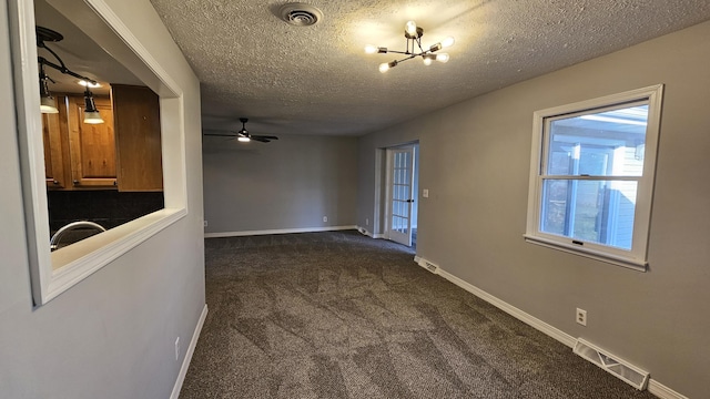 empty room featuring sink, ceiling fan with notable chandelier, dark carpet, and a textured ceiling