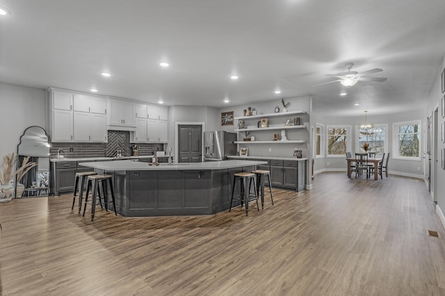 kitchen with gray cabinetry, a kitchen island with sink, stainless steel refrigerator with ice dispenser, decorative backsplash, and light wood-type flooring