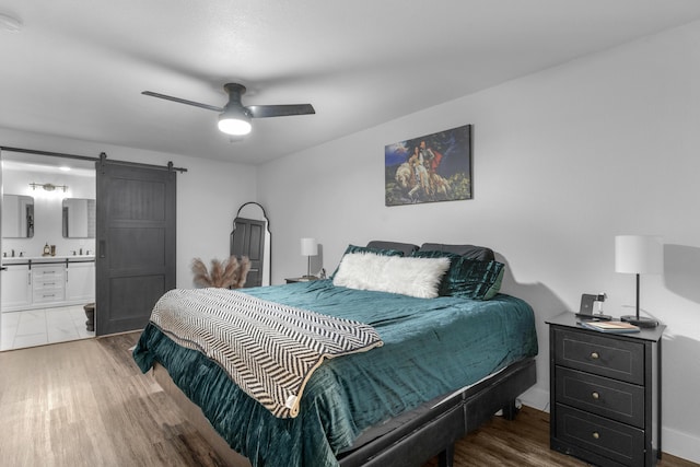 bedroom with a barn door, ceiling fan, ensuite bathroom, and dark hardwood / wood-style floors