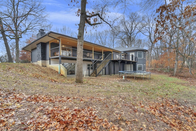 rear view of house featuring a trampoline and a wooden deck