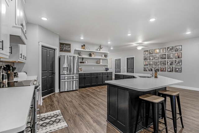 kitchen featuring white cabinetry, stainless steel fridge, an island with sink, wood-type flooring, and a breakfast bar