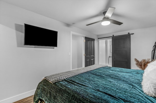 bedroom featuring ceiling fan, a barn door, and wood-type flooring