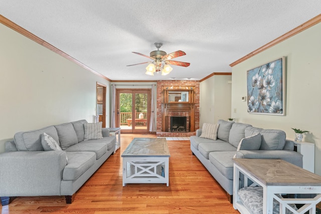 living room with a textured ceiling, ceiling fan, crown molding, light hardwood / wood-style flooring, and a fireplace