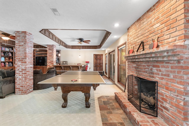 playroom with a brick fireplace, ceiling fan, decorative columns, and a tray ceiling