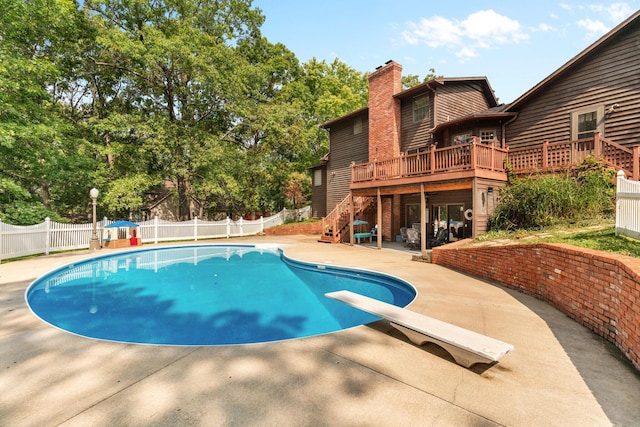 view of swimming pool featuring a wooden deck, a diving board, and a patio