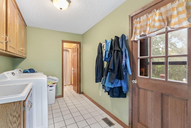 laundry room featuring washing machine and clothes dryer, light tile patterned floors, cabinets, and a textured ceiling