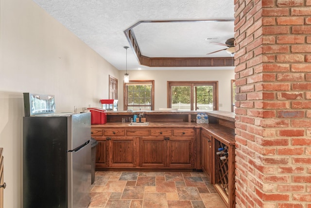 kitchen with kitchen peninsula, a textured ceiling, a tray ceiling, stainless steel refrigerator, and hanging light fixtures