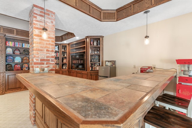 bar with a tray ceiling, tile counters, hanging light fixtures, and a textured ceiling