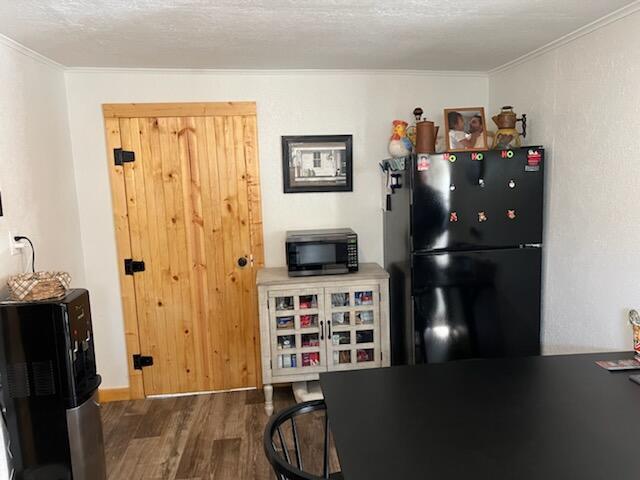 kitchen featuring black refrigerator, dark wood-type flooring, a textured ceiling, and ornamental molding