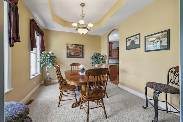 carpeted dining space featuring an inviting chandelier and a raised ceiling