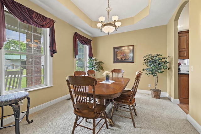 carpeted dining space with a raised ceiling and a notable chandelier