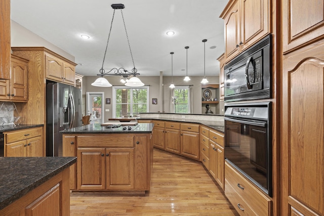 kitchen with kitchen peninsula, light wood-type flooring, dark stone counters, black appliances, and pendant lighting