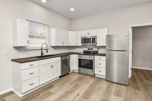 kitchen featuring appliances with stainless steel finishes, butcher block countertops, white cabinetry, and sink