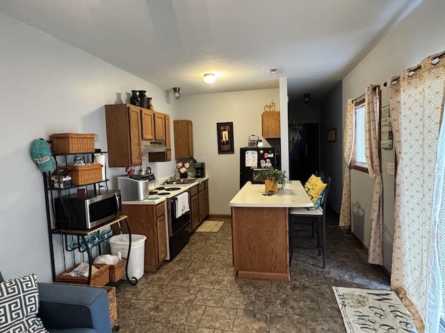 kitchen featuring white range with electric cooktop, black fridge, sink, a kitchen island, and a kitchen bar