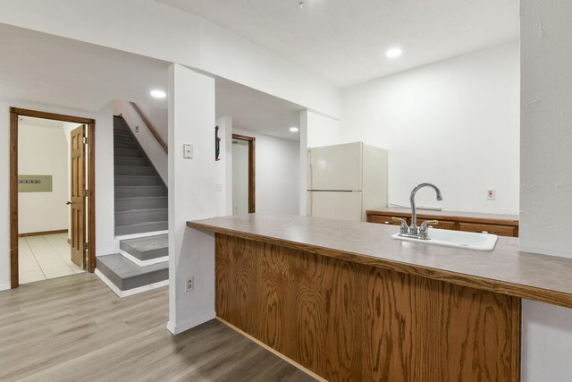 kitchen with kitchen peninsula, white fridge, light wood-type flooring, and sink