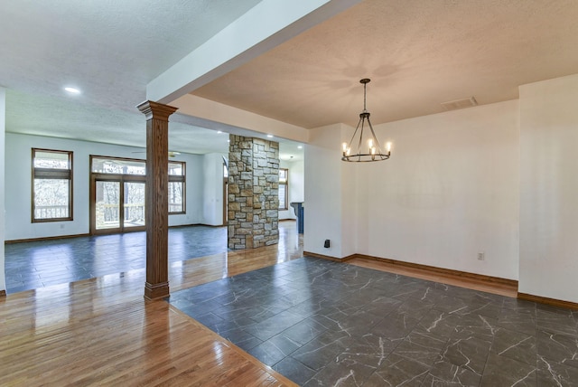 unfurnished room featuring ornate columns, a textured ceiling, and a chandelier