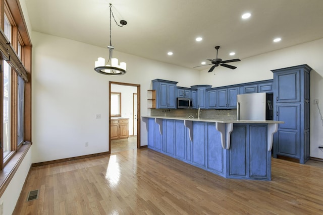 kitchen with blue cabinetry, stainless steel appliances, backsplash, pendant lighting, and a kitchen bar