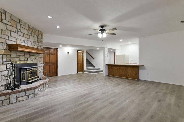 unfurnished living room with a wood stove, ceiling fan, sink, and light hardwood / wood-style floors