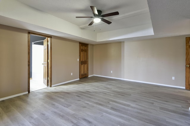 empty room featuring a tray ceiling, ceiling fan, light hardwood / wood-style floors, and a textured ceiling