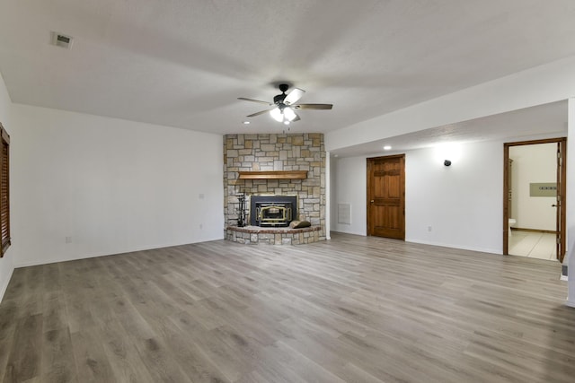 unfurnished living room with a textured ceiling, light hardwood / wood-style floors, a wood stove, and ceiling fan