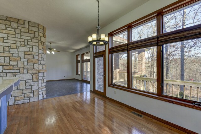 interior space featuring ceiling fan with notable chandelier, a healthy amount of sunlight, and wood-type flooring