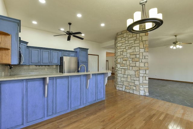 kitchen with appliances with stainless steel finishes, dark hardwood / wood-style flooring, ornate columns, blue cabinets, and a breakfast bar area