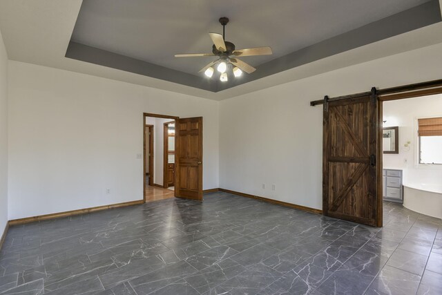 spare room with ceiling fan, a barn door, and a tray ceiling