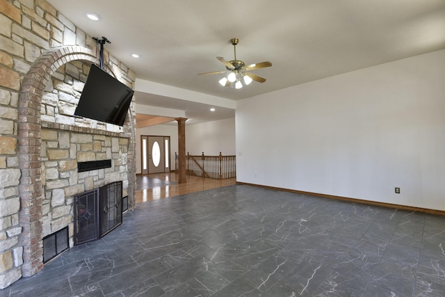 unfurnished living room featuring decorative columns, a stone fireplace, and ceiling fan