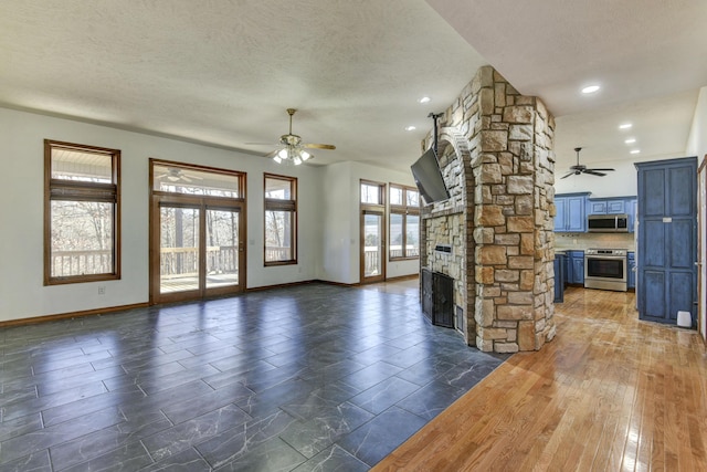 unfurnished living room featuring a textured ceiling, a stone fireplace, ceiling fan, and a healthy amount of sunlight