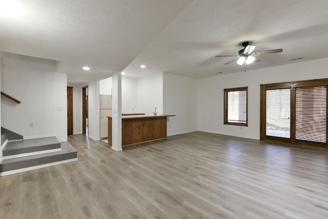 unfurnished living room with ceiling fan, a textured ceiling, and light hardwood / wood-style flooring