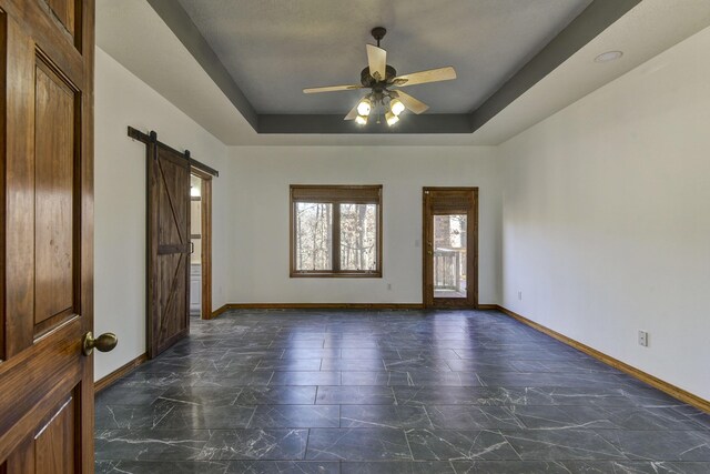 unfurnished room featuring ceiling fan, a barn door, and a raised ceiling