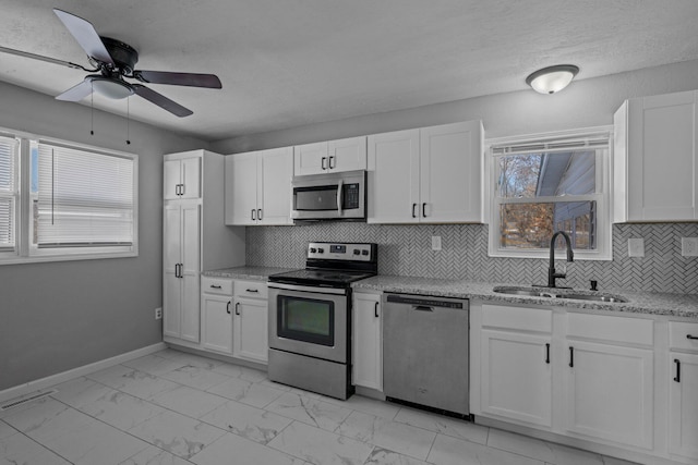 kitchen featuring stainless steel appliances, sink, white cabinetry, ceiling fan, and decorative backsplash