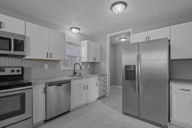 kitchen with light stone counters, stainless steel appliances, white cabinets, and sink