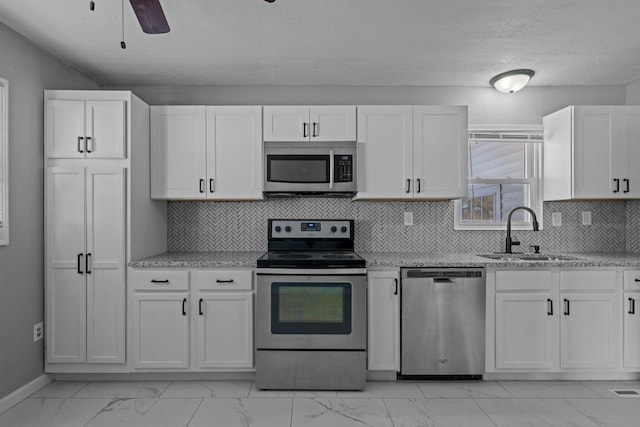 kitchen featuring light stone countertops, stainless steel appliances, white cabinetry, ceiling fan, and sink