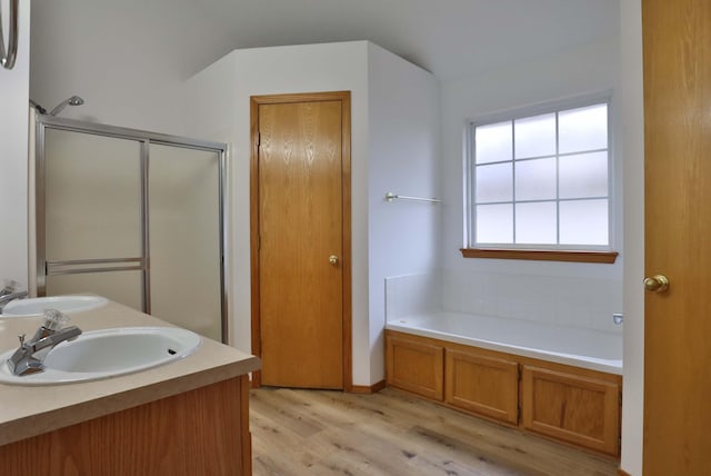 bathroom featuring vanity, wood-type flooring, plus walk in shower, and vaulted ceiling