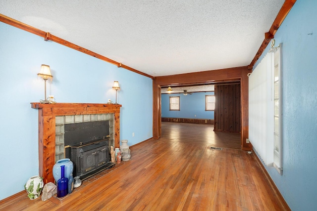 unfurnished living room featuring a wood stove, ceiling fan, hardwood / wood-style floors, a textured ceiling, and ornamental molding