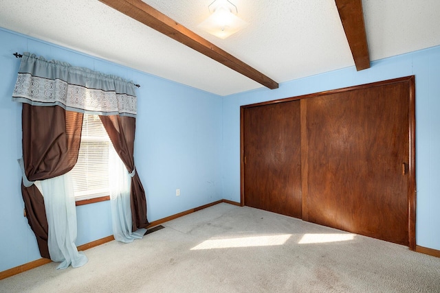 unfurnished bedroom with beamed ceiling, a textured ceiling, light colored carpet, and a closet