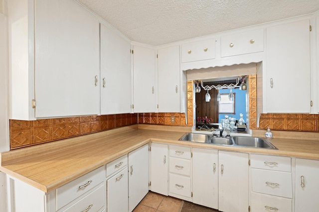 kitchen with white cabinets, light tile patterned floors, sink, and a textured ceiling