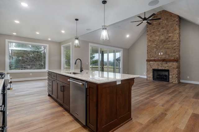 kitchen with light stone countertops, sink, a center island with sink, a stone fireplace, and hanging light fixtures