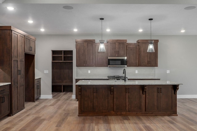 kitchen featuring a center island with sink, dark brown cabinets, light stone countertops, and hanging light fixtures