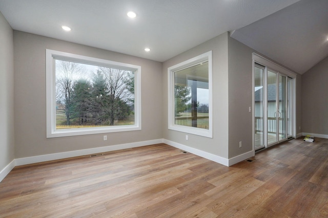 unfurnished room with a healthy amount of sunlight, vaulted ceiling, and light wood-type flooring