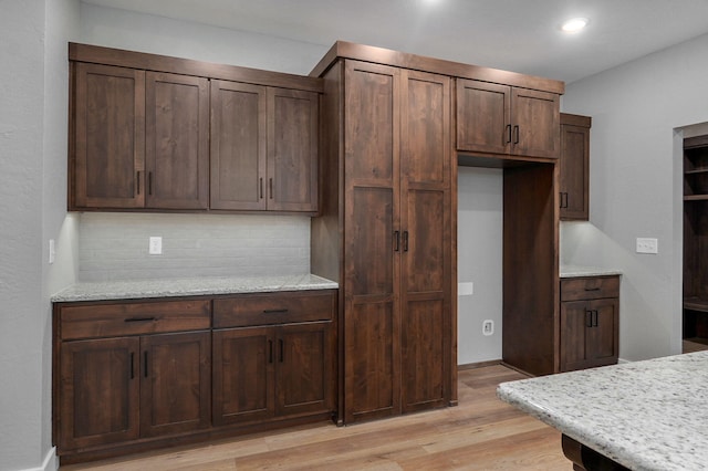 kitchen featuring dark brown cabinetry, tasteful backsplash, light stone counters, and light hardwood / wood-style floors