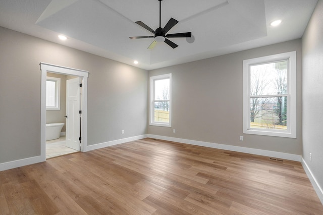 unfurnished bedroom with multiple windows, ensuite bathroom, light hardwood / wood-style flooring, and ceiling fan