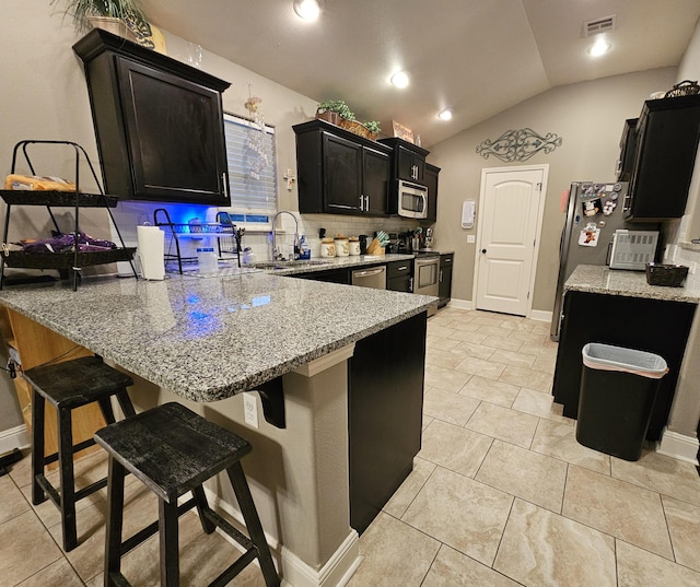 kitchen with lofted ceiling, a kitchen breakfast bar, sink, appliances with stainless steel finishes, and light stone counters