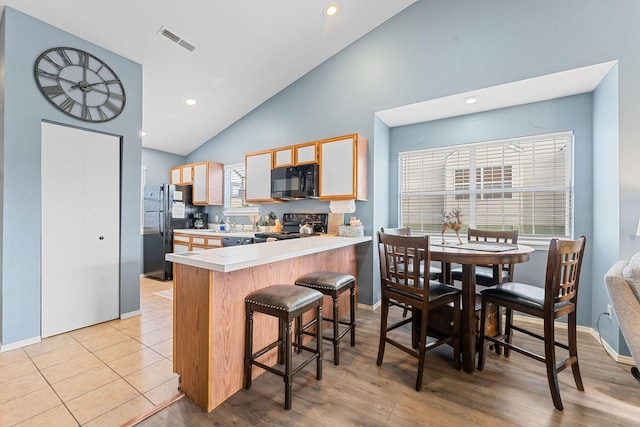 kitchen with kitchen peninsula, light wood-type flooring, black appliances, high vaulted ceiling, and a breakfast bar area